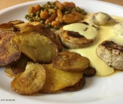Schweinemedaillons mit Bratkartoffeln, Erbsen und Möhrchen und Soße Hollandaise in Nahaufnahme