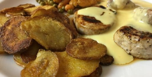 Schweinemedaillons mit Bratkartoffeln, Erbsen und Möhrchen und Soße Hollandaise in Nahaufnahme