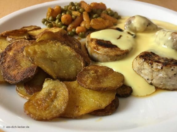 Schweinemedaillons mit Bratkartoffeln, Erbsen und Möhrchen und Soße Hollandaise in Nahaufnahme