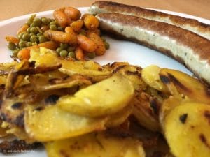 Geflügelbratwurst, Bratkartoffeln mit Erbsen und Möhren in Nahaufnahme