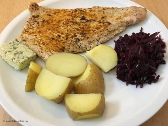 Putenschnitzel mit Pellkartoffeln und Rotkohl auf einem weissen Teller serviert