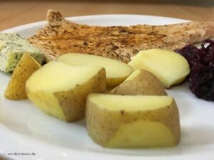 Putenschnitzel mit Pellkartoffeln und Rotkohl in Nahaufnahme auf einem weissen Teller serviert